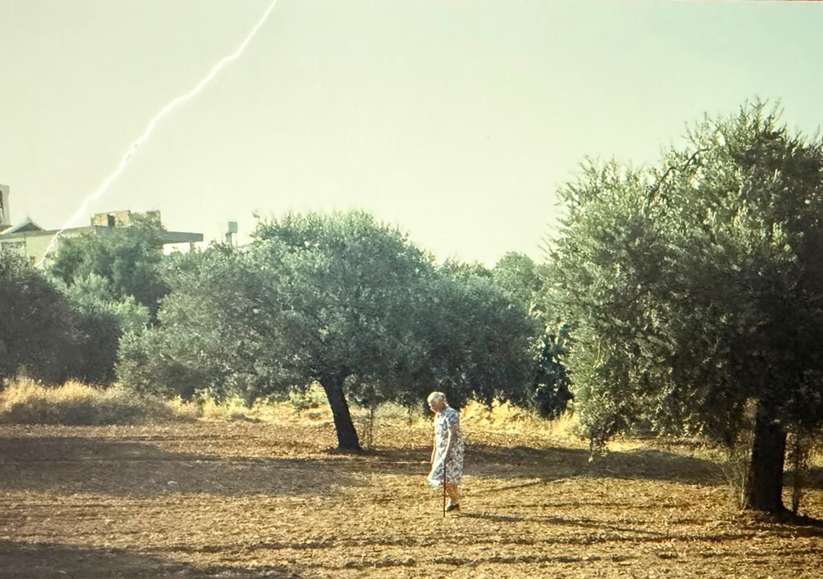 Maritsa walking her olive grove at Kampia, the village church behind her. Family archive photograph.
